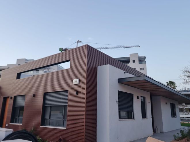 חיפוי אלומיניום דמוי עץ עוטף פינת מבנה, עם הצללת כניסה באותו גוון